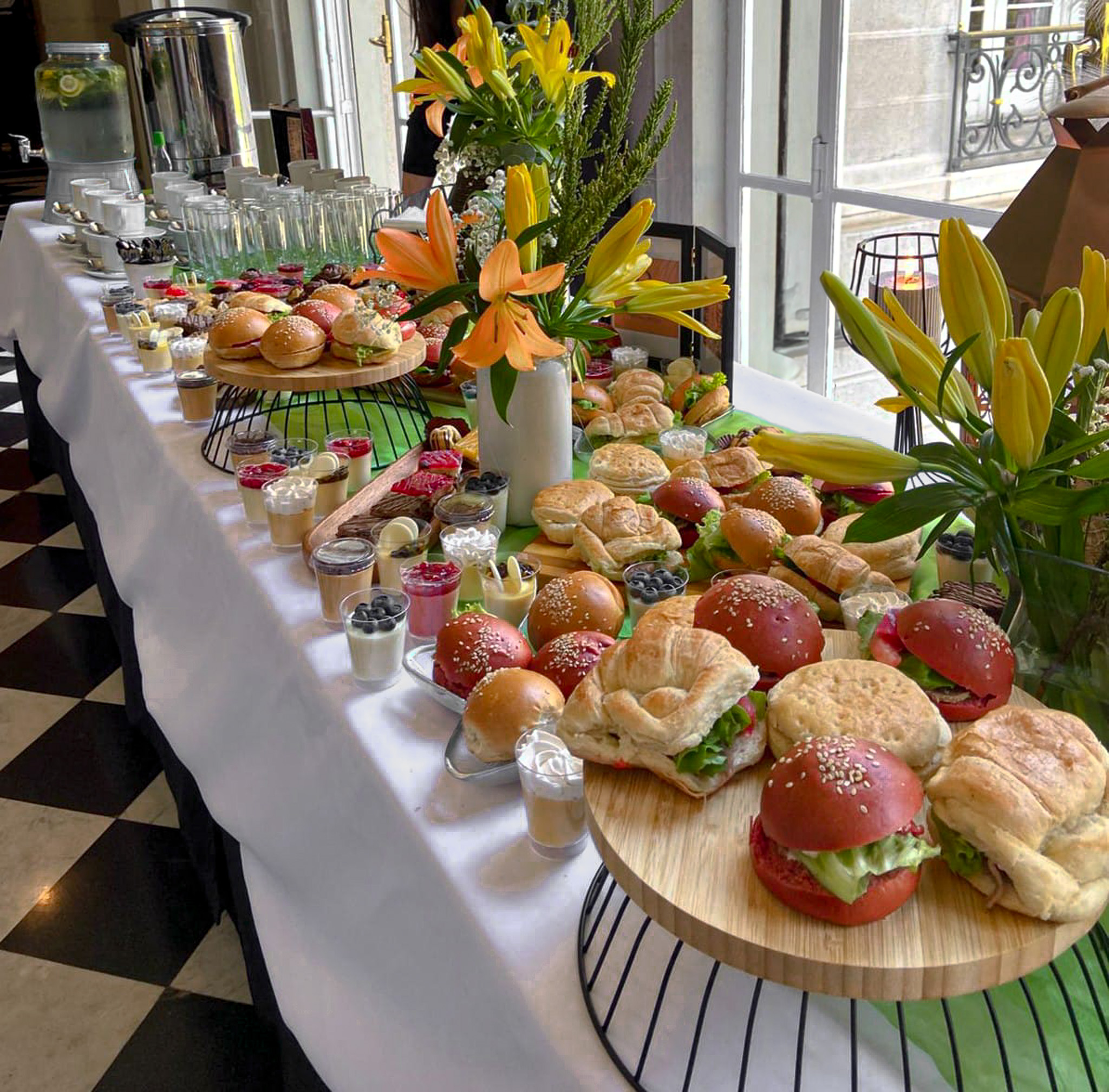 Mesa de brunch con mini sándwiches, postres y flores